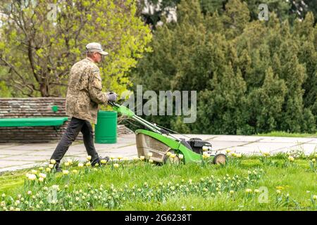 Kiev, Ukraine - 27 avril 2021 : un homme avec une tondeuse tond l'herbe dans le parc. Banque D'Images