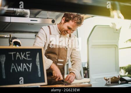 Jeune chef cuisinant dans le restaurant camion de nourriture vegan - Focus sur le visage Banque D'Images