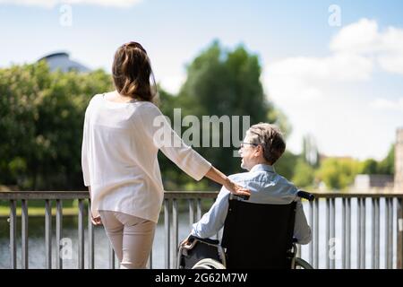 Soins aux personnes âgées et transport en fauteuil roulant. Femme souriante poussant l'homme âgé Banque D'Images