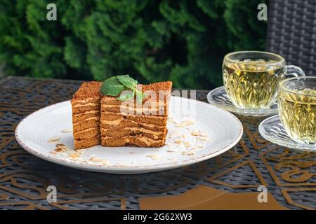 Morceaux de gâteau et deux tasses en verre de thé à la menthe. Gâteau Medovik sur une table dans un café d'été. Concept de boisson au thé, culture russe. Encore la vie. Maison h Banque D'Images