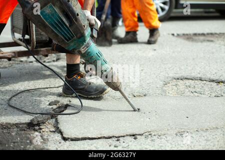 Il enlève l'asphalte avec un marteau à inertie. Retrait de la couche d'asphalte de la route. Le travailleur tient un marteau à inertie. Réparation sur route. Utilisation d'un hammam électrique Banque D'Images