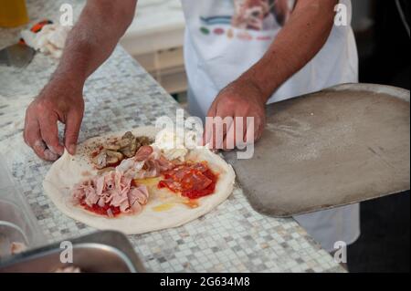 Pizziolo met une pizza quatre saisons sur le pelage, prêt à cuire. Banque D'Images