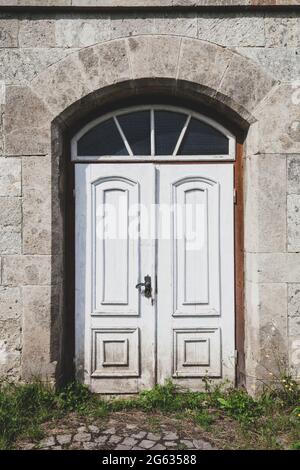 Ancienne porte en bois blanc abandonnée dans la maison à la rue de la ville. Ancienne porte en bois fermée dans le mur en pierre du cottage Banque D'Images