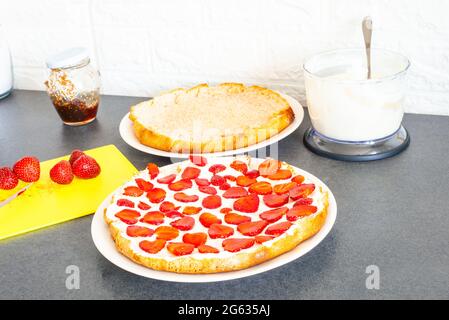 Processus de fabrication de gâteau fait maison avec de la crème blanche et des tranches de fraises sur l'assiette. Préparation de la pâte molle avec des baies rouges fraîches et de la crème au fromage à faire Banque D'Images