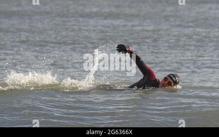 Man Wild Swimming en utilisant la couverture avant dans la mer portant UN costume humide, chapeau et Googles, Avon Beach UK Banque D'Images