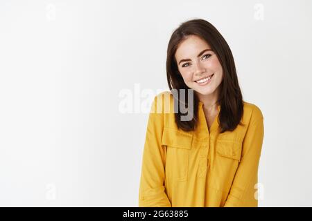 Image d'une femme mignonne et romantique qui regarde la caméra, souriant et timide, debout sur fond blanc Banque D'Images