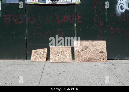 Des dessins abandonnés, sans surveillance et apparemment libres sur du carton ont été proptés contre un mur avec des graffitis sur Steinway Street à Astoria, Queens, New York. Banque D'Images