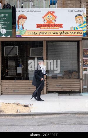 Un juif hassidique marche près de la réserve une bibliothèque de livres sur Lee Avenue à Williamsburg, Brooklyn, New York. Banque D'Images