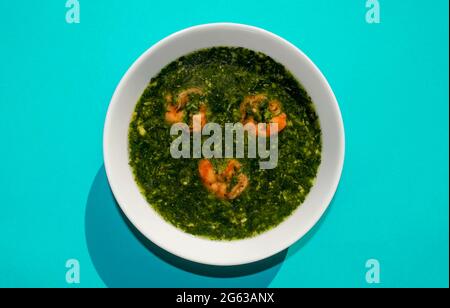 Célèbre cuisine arabe traditionnelle. Soupe verte Molokhia aux crevettes sur fond bleu. Flat lay, vue de dessus. Moroheiya Banque D'Images