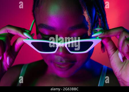 Belle jeune femme africaine portant des lunettes de soleil élégantes isolées sur fond bleu. Banque D'Images