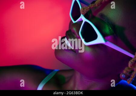 Belle jeune femme africaine portant des lunettes de soleil élégantes isolées sur fond bleu. Banque D'Images