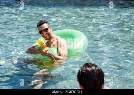 homme arabe enthousiaste qui s'amuse avec un pistolet à eau et une piste de natation dans la piscine Banque D'Images