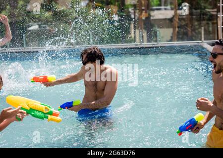 des amis multiethniques enthousiastes qui se battent sur des pistolets à eau dans la piscine Banque D'Images