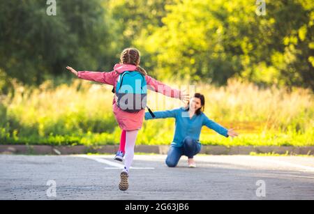 Vue arrière d'une fille d'école qui court à la mère après le cours dans une rue ensoleillée Banque D'Images