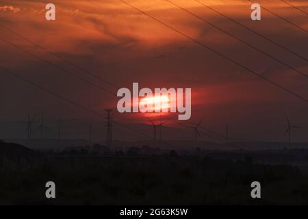 Un immense soleil rouge se couche derrière les nuages et un paysage de câbles et d'éoliennes dans la vallée de l'Ebre, près de la ville de Gallur, Aragon, Espagne Banque D'Images