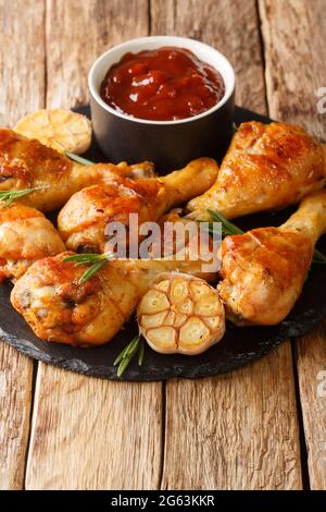 Des cuisses de poulet grillées à l'ail et au romarin servies avec une sauce barbecue en gros plan sur un tableau d'ardoise sur la table. Verticale Banque D'Images