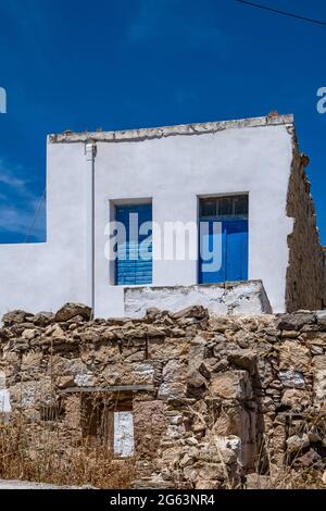 Cyclades Grèce. Petite maison blanche avec porte et fenêtre de couleur bleue, cadres en bois sur mur blanchi à la chaux à Kimolos, architecture de l'île grecque, ciel bleu Banque D'Images