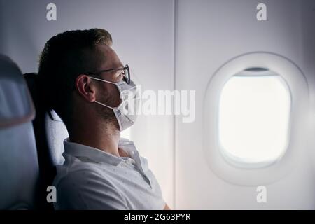 Passager avec masque de protection. Jeune homme homme regardant par la fenêtre de l'avion. Thèmes voyageant dans la nouvelle norme et la protection personnelle pendant pande Banque D'Images