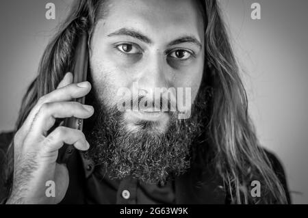 portrait noir et blanc d'un jeune homme d'affaires du moyen-orient avec une barbe et de longs cheveux tout en ayant une conversation sur le téléphone portable Banque D'Images