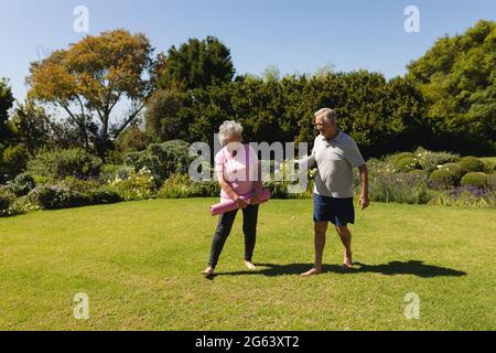 Couple caucasien senior tenant des tapis de yoga et souriant dans le jardin ensoleillé Banque D'Images