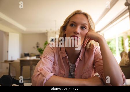 Femme caucasienne assise à une table travaillant dans le salon, s'appuyant sur le bureau pendant un appel vidéo Banque D'Images