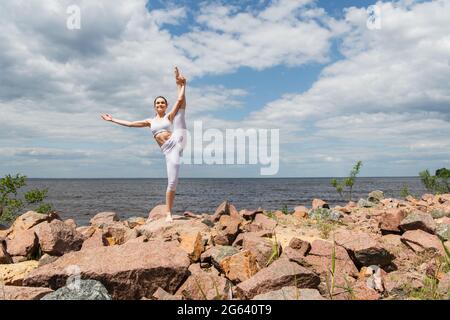 une femme heureuse dans les vêtements de sport debout main à gros orteil pose près de la mer Banque D'Images