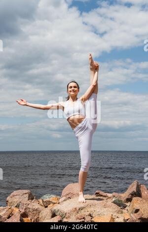 femme gaie dans les vêtements de sport debout main à gros orteil pose près de la mer Banque D'Images