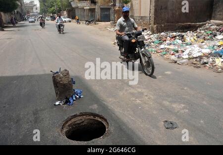 Les navetteurs passent à proximité d'un trou d'égout principal ouvert qui peut causer tout accident particulièrement dans les heures de nuit, montrant la négligence des départements concernés, sur la route Risala à Hyderabad le vendredi 02 juillet 2021. Banque D'Images