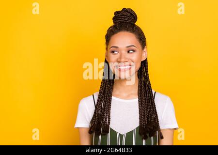 Photo de brillant charmante peau sombre dame porter des vêtements décontractés regardant l'espace vide souriant isolé couleur jaune arrière-plan Banque D'Images