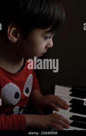 enfant jouant du piano portant une chemise orange. arrière-plan vertical sombre Banque D'Images