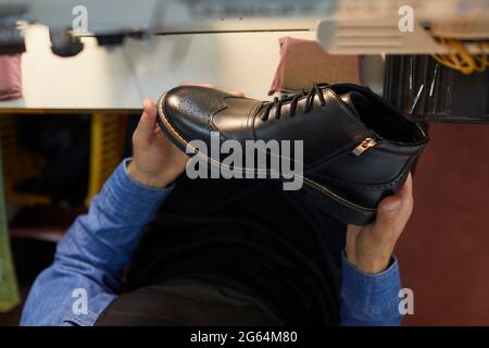 Gros plan à grand angle de la nouvelle chaussure en cuir noir dans les mains du travailleur de l'usine de chaussures Banque D'Images