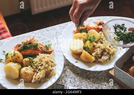 Saumon cuit au four avec chou cuit et pommes de terre neuves avec aneth. Femme servant le dîner. Banque D'Images