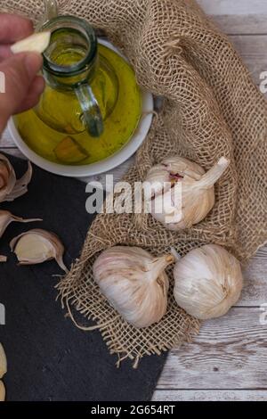 détail de la production de l'huile d'olive aromatique et une personne versant des morceaux d'ail coupés avec des têtes d'ail sur un toile de toile de jute avec un foyer sélectif Banque D'Images