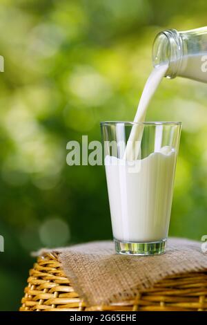 le lait coule du biberon dans le verre à l'extérieur Banque D'Images