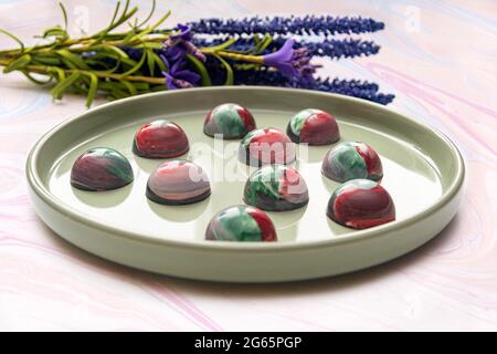 Bonbons au chocolat trempé à la main de collection avec un corps peint brillant sur une plaque ronde avec un fond flou et des éléments bokeh. Stock photog Banque D'Images