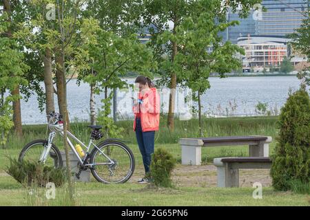 Biélorussie, Minsk - 28 mai 2021 : une femme avec un vélo se repose dans le parc et regarde dans un smartphone. Photos. Banque D'Images