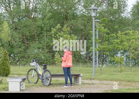 Biélorussie, Minsk - 28 mai 2021 : une femme avec un vélo se repose dans le parc et regarde dans un smartphone. Photos. Banque D'Images