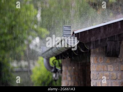 Forte pluie tombant sur le toit et caniveau métallique de la maison en brique en été Banque D'Images