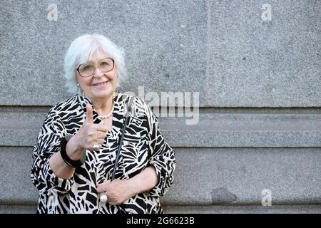 femme plus âgée regardant dans l'appareil photo avec les pouces à l'extérieur Banque D'Images