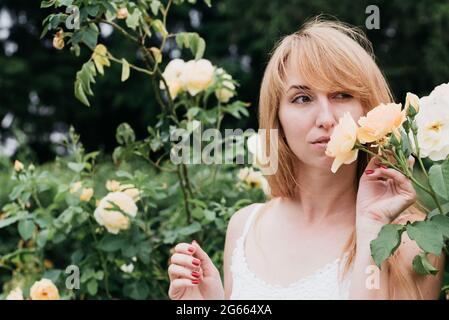 Printemps et été. Jeune femme adorable blonde sniffing arôme de fleur rose. Parfums et cosmétiques. Fleurs de roses sauvages. Concept de jardin secret. Banque D'Images