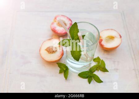 Thé glacé rafraîchissant à la menthe poivrée et pêches sur fond gris, concentration sélective. Boisson à l'eau avec pêches Banque D'Images