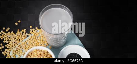 Lait de soja mélangé au sésame noir dans du verre transparent sur un tapis noir. Graines de sésame noir et graines de soja dans une tasse. Lait mélangé de soja de sésame noir. Il Banque D'Images