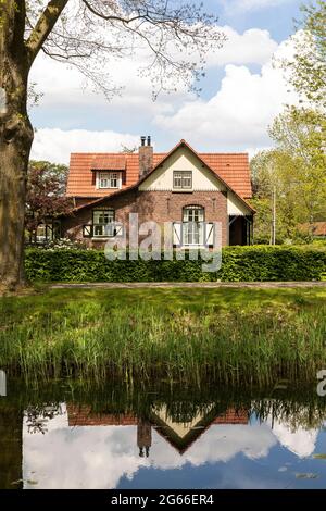 Ancienne maison typique hollandaise authentique près de la rivière avec des reflets dans l'eau, entourée d'arbres et de verdure par une journée ensoleillée au printemps à Grien Banque D'Images