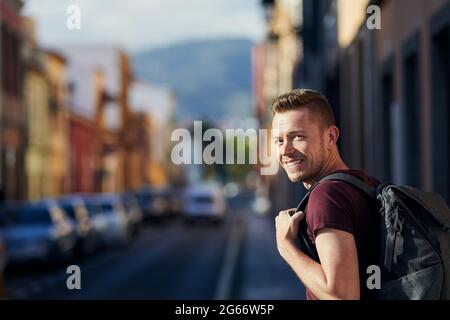Heureux voyageur seul regardant l'appareil photo. Homme souriant avec sac à dos dans la rue de la vieille ville. San Cristóbal de la Laguna à Tenerife, Iles Canaries, Espagne. Banque D'Images