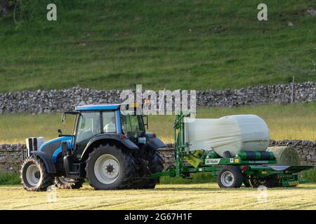 Envelopper une balle ronde d'ensilage avec un film de protection en plastique, North Yorkshire, Royaume-Uni. Banque D'Images