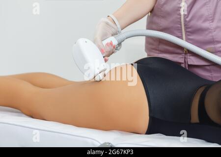 Épilation au laser en action. Cosmetologiste en train de réaliser une épilation au laser sur les fesses de la jeune femme. Une maniple en gros plan dans le salon de spa Banque D'Images