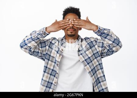 Portrait d'un jeune homme afro-américain élégant proche des yeux, couverture avec les mains, attente de surprise, debout les yeux bandés, anticipation smth, debout Banque D'Images