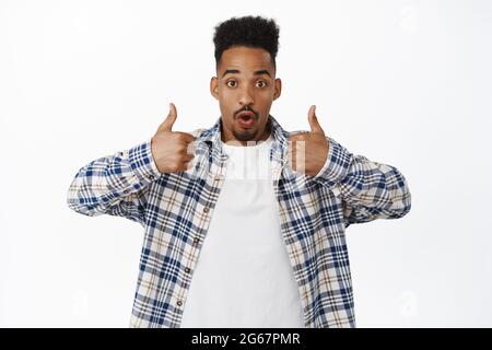 Impressionné jeune homme afro-américain montrant le pouce et regarder surpris à l'appareil photo, le taux smth impressionnant, les commentaires positifs bonne, louange événement étonnant Banque D'Images