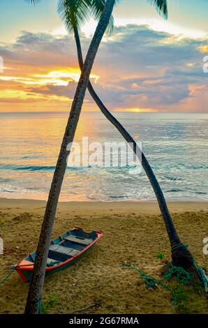 Coucher de soleil sur une plage portoricaine avec palmiers et bateau de pêche traditionnel. Rincon, PR. Banque D'Images