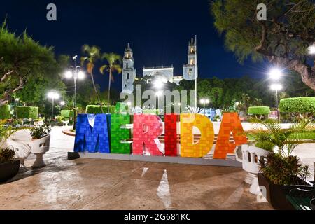 Grandes lettres colorées représentant Merida avec une cathédrale emblématique de Merida en arrière-plan la nuit. Banque D'Images